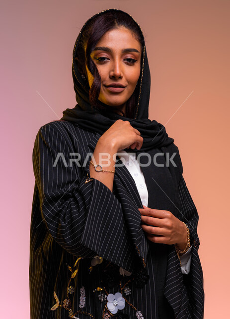 Wearing the latest designs of Saudi and international women's clothing and accessories, interest in beauty and elegance, a close-up portrait of a smiling Saudi Arabian Gulf woman wearing a black striped cloak and a golden bracelet, following fashion news 