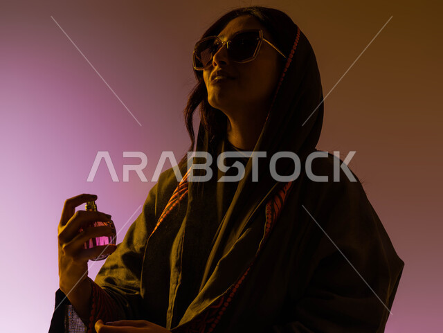 تجربة فريدة لإحدى العطور، التسويق لمنتجات العطور النسائيه الخليجيه والعالمية، بورتريه مقرب لإمرأه عربيه سعودية خليجية ترتدي العباءة العصرية والنظارات الشمسية تقوم برش العطر، استخدام الزيوت العطرية الطبيعية، التطيب والتعطر بالعود العطري، خلفية ملونة