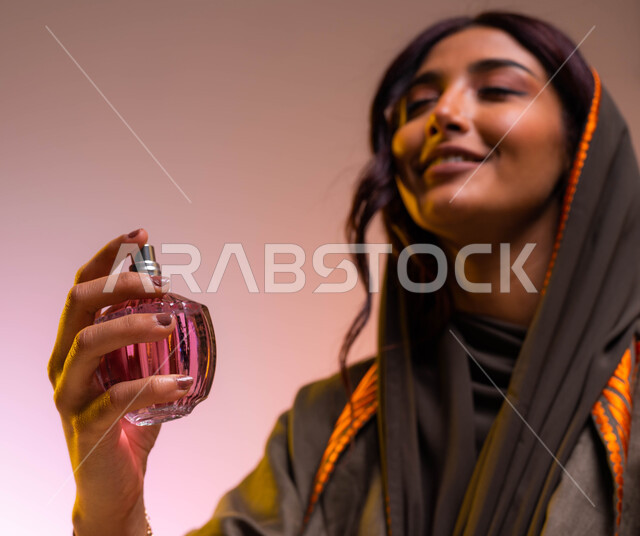 استخدام الزيوت العطرية الطبيعية، التسويق لمنتجات العطور النسائيه الخليجيه، بورتريه مقرب لإمرأه عربيه سعودية خليجية ترتدي عباءة بنية مطرزة تقوم برش العطر، مفهوم الأناقة والإهتمام بالمظهر الخارجي، التطيب والتعطر بالعود العطري، خلفية ملونة
