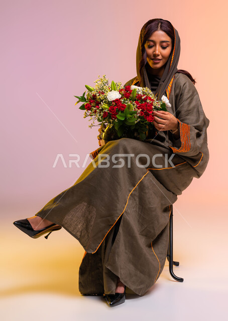 إنتقاء الباقة الأجمل من الورود، متاجر ومراكز بيع وشراء باقات الأزهار والهدايا في الأعياد والمناسبات السعيدة، بورتريه لسيدةعربية خليجية سعودية ترتدي عباءة بنية مطرزة عصرية تحمل بيدها  حوض من الورد الفاخر، الاهتمام بالاناقه و المظهر الخارجي، خلفية ملونة