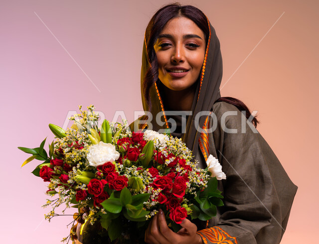 Owning bouquets of flowers on holidays and happy occasions, gestures indicating joy and happiness, a close-up portrait of a smiling Saudi Gulf Arab young woman wearing a brown embroidered cloak holding a bouquet of roses in her hand, shops and stores buyi