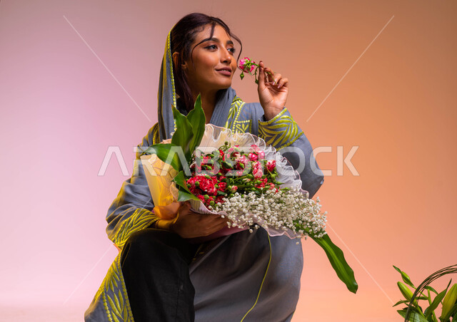 محلات ومتاجر بيع وشراء الزهور الطبيعية، امتلاك باقات الورود والهدايا في الأعياد والمناسبات السعيدة، بورتريه لشابة عربية خليجية سعودية ترتدي العباءة العصرية تقوم بشم رائحة الزهور، إيماءات الإعجاب بالروائح العطرية الزكية للورد، خلفية ملونة