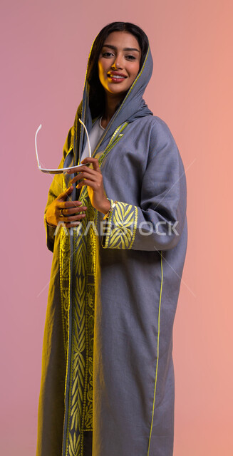 Display of modern fashion and clothing, designs of models of modern Saudi women's abayas, the concept of elegance and concern for external appearance, gestures of femininity and kindness, portrait of a smiling Saudi Arab Gulf woman holding sunglasses, buy