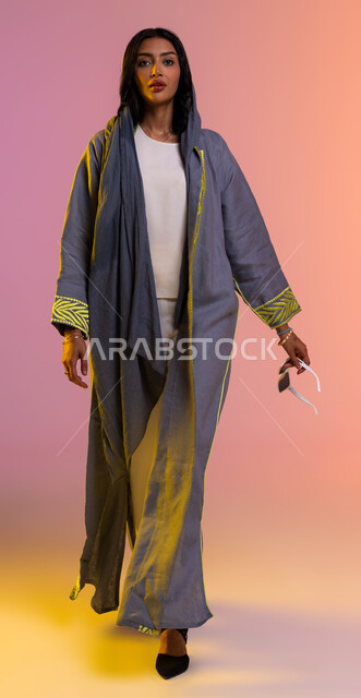 ايماءات تدل على الثقة بالنفس, عرض تصاميم العباءات السعودية, بورتريه لعارضة أزياء عربية خليجية ترتدي عباية ملونة أنيقة, شراء الملابس والاكسسوارات الجديدة, صورة الجسم بالطول الكامل, خلفية ملونة