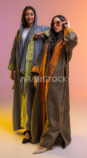 ارتداء نظارات شمسية عصرية وعباءات خليجية نسائية أنيقة، منتجات نسائية سعودية, ايماءات الصداقة والمحبة, بورتريه لصديقتان عربيتان خليجيتان سعوديتان، مفهوم الموضة والأناقة، شراء الملابس والاكسسوارات الجديدة، الجسم بالطول الكامل, خلفية ملونة