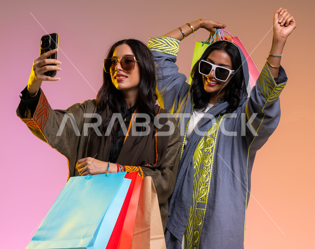 إيماءات الفرحه بعد التسوق، التسوق الممتع مع الاصدقاء، عباءات خليجيه نسائيه عصريه، بورتريه لصديقتان عربيتان خليجيتان سعوديتان، مفهوم الموضه والأناقه، ارتداء النظرات الشمسيه، شراء الملابس و الاكسسوارات النسائيه، خلفيه ملونة