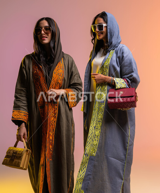 Going shopping and buying bags with friends, a portrait of two Saudi Arabian Gulf women, wearing the modern Gulf abaya and sunglasses, Saudi women's products, spending fun times with girlfriends, a colorful background