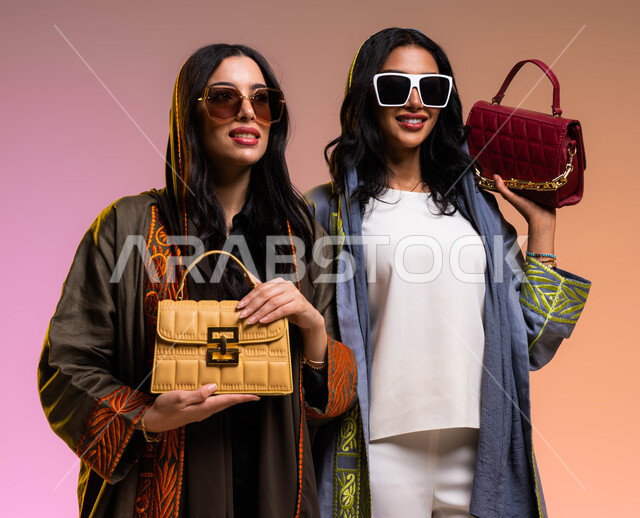 حقائب عصرية وموديلات مختلفة, منتجات نسائيه سعوديه، بورتريه لإمرأتان عربيتان سعوديتان خليجيتان، عباءات خليجية أنيقه، ايماءات تدل على الانوثة والجمال، ارتداء النظارات الشمسية، مفهوم الموضه والأناقة، خلفية ملونة
