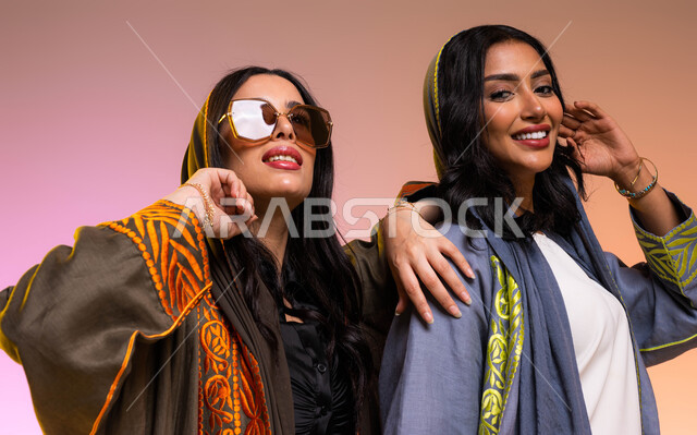 عرض الأزياء والموديلات الحديثة، مفهوم الموضة والأناقة، عباءات خليجية نسائية عصرية، ايماءات الصداقه واللطافه لرفيقتين عربيتين خليجيتين سعوديتين، ارتداء النظارات الشمسية، شراء الملابس والاكسسوارات النسائية الجديدة، خلفية ملونة