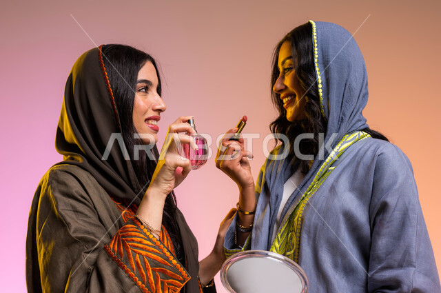 مستحضرات نسائيه عالميه، مفهوم الأناقة والإهتمام بالمظهر الخارجي، بورتريه لصديقتان عربيتان سعوديتان خليجيتان تستمتعان بالتزيين النسائي, التطيب والتعطر بالعود والزيوت العطرية، الشغف بوضع أحمر الشفاه، خلفية ملونة