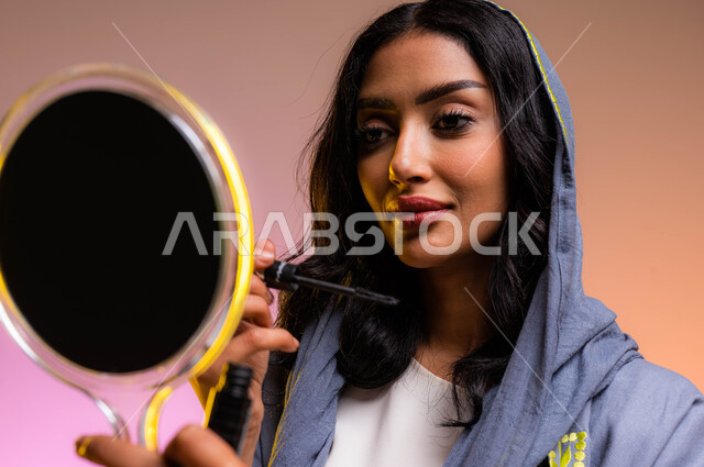 Marketing of cosmetic products and cosmetics in stores and on the Internet, the concept of caring for beauty and skin, a portrait of a Saudi Arabian Gulf beautician holding a makeup tool (mascara pen) to highlight the eye and looking at the mirror, toreal