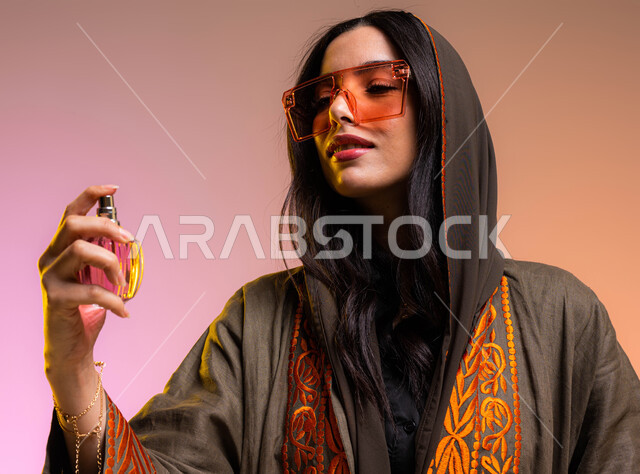 التطيب والتعطر بالعود والزيوت العطرية, مفهوم الأناقة والإهتمام بالمظهر الخارجي, بورتريه مقرب لإمرأة عربية سعودية خليجية تقوم برش العطر, التسويق لمنتجات العطور والمستحضرات النسائية, ارتداء العباءة والنظارات الشمسية, خلفية ملونة