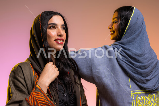 ايماءات تدل على الصداقة والمحبة, عباءات خليجية نسائية عصرية, بورتريه لصديقتان عربيتان سعوديتان خليجيتان, مفهوم الموضة والأناقة, تعابير وجه تدل على السعادة, عرض الأزياء والموديلات الجديدة, خلفية ملونة