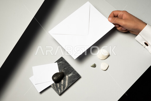 موك اب لاوراق ملاحظات صغيرة على الطاولة، صورة مقربة ليد رجل عربي سعودي خليجي يمسك بمظروف رسائل، ادوات وقرطاسية مكتبية