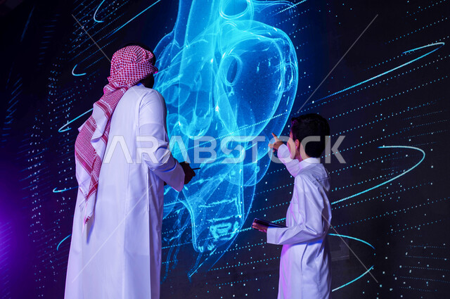 شرح وتوضيح مخطط أعضاء جسم الإنسان بالتكنولوجيا العلمية المتطورة، طالب ومدرس عربيان خليجيان سعوديان يستخدمان جهاز التابليت، دمج التعليم مع التقنية، التعليم المتطور بإستخدام شاشات هولوجرامية ثلاثية الأبعاد لقلب الإنسان، رؤية مستقبلية 2030