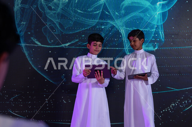 استخدام التقنيات الحديثة في رحلة التعليم، تنمية التفكير العلمي لدى الطلاب في المختبرات العلمية، طالبان سعوديان عربيان خليجيان يستخدمان اجهزة التابليت، خلفية شاشات هولوجرامية ثلاثية الأبعاد لقلب الإنسان، رؤية مستقبلية 2030