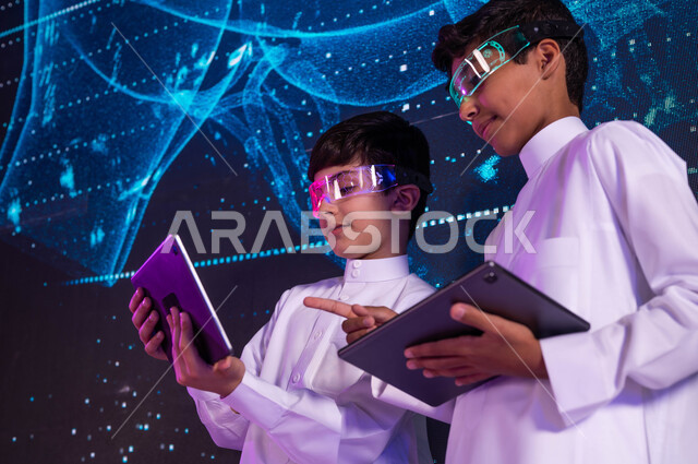 تنمية التفكير العلمي لدى الطلاب في المختبرات العلمية، طالبان سعوديان عربيان خليجيان يرتديان نظارات الواقع الافتراضي ويستخدمان اجهزة التابليت، خلفية شاشات هولوجرامية ثلاثية الأبعاد لقلب الإنسان، رؤية مستقبلية 2030