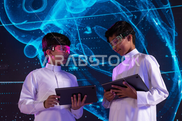 ابتكار اساليب حديثة في التعليم، خلفية شاشات هولوجرامية ثلاثية الأبعاد لقلب الإنسان، طالبان سعوديان عربيان خليجيان يرتديان نظارات الواقع الافتراضي ويستخدمان اجهزة التابليت، مخطط أعضاء جسم الإنسان بالتكنولوجيا العلمية المتطورة، رؤية مستقبلية 2030