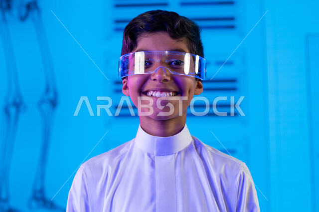 أساليب وإستراتيجيات جديدة في نظام  التعليم في المدارس السعودية، طالب عربي سعودي خليجي مبتسم يرتدي نظارات الواقع الإفتراضي وينظر للكاميرا، إيماءات وجه تدل على السعادة، التعليم المتطور بإستخدام شاشات إلكترونية وتقنيات حديثة، رؤية مستقبلية 2030
