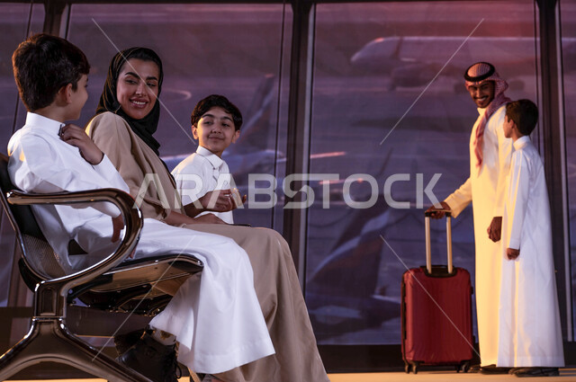 حوارات ونقاشات الأم مع أبنائها، عائلة عربية سعودية خليجية في قاعة الانتظار في المطار، رجل يرتدي الزي السعودي التقليدي ويمسك حقيبة سفر حمراء، إيماءات السعادة للسفر والسياحة، رحلة عائلية صيفية ممتعة, الاستعداد لركوب الطائره