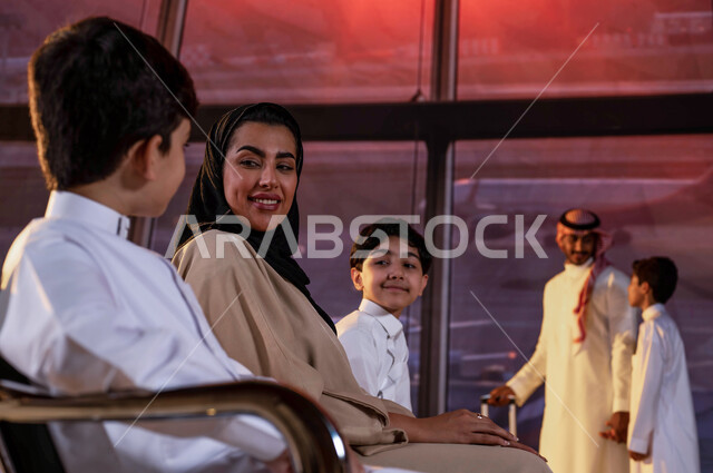 إيماءات تدل على السعادة و الحماس للسفر، عائلة عربية خليجية سعودية في صالة المطار، السياحة و السفر الجوي مع الأبناء, الإستعداد لركوب الطائرة في قاعة الإنتظار، رحلات جوية عائلية، قضاء رحلة صيفية ممتعة، إرتداء الزي السعودي التقليدي