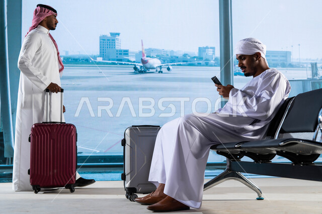 تجمع الركاب داخل صالة الانتظار في المطار, رجل مصري يرتدي الجلابيه والعمامة ويستخدم الهاتف المحمول, رجل عربي خليجي سعودي يرتدي الشماغ والثوب السعودي التقليدي يمسك بيده حقيبة السفر  وينتظر ركوب الطائرة, النظر إلى الطائرات عبر النافذة, رحلات سياحية ممتعة