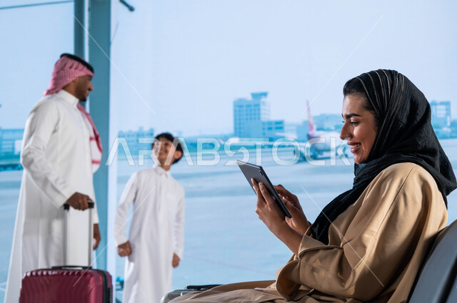 إيماءات تدل على السعادة والفرح, دردشات ومحادثات وتواصل اجتماعي عبر جهاز التابليت, عائلة عربية سعودية خليجية في قاعة الانتظار في المطار، الاستعداد للسفر والسياحة الترفيهيه في السعودية، قضاء عطلة صيفية ممتعة برفقة العائلة