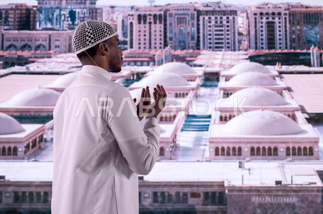 التصاميم المعمارية الإسلامية لقباب المساجد في المدينة المنورة, فضل الصلاة والدعاء في مسجد رسول الله, صورة من الخلف لرجل عربي سعودي خليجي يرتدي الزي السعودي يقف أمام المسجد النبوي الشريف ويدعو الله تعالى, خلفية القبب لمسجد النبي محمد عليه الصلاة والسلام