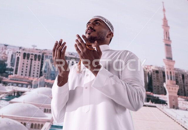 خلفية المئذنة والقبب لمسجد النبي محمد صلى الله عليه وسلم، فضل الصلاة و الدعاء في مسجد رسول الله، رجل مسلم عربي سعودي خليجي يقف أمام المسجد النبوي الشريف ويدعو الله تعالى، العمارة الاسلامية العريقة لقباب المساجد في المدينة المنورة