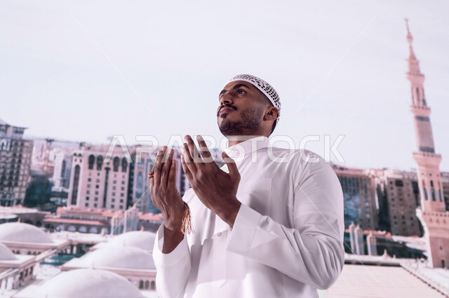اسلاميات وعبادات, فضل الصلاة والدعاء في مسجد نبي الله، رجل عربي سعودي خليجي يرتدي الثوب السعودي يقف أمام  المسجد النبوي الشريف ويدعو الله تعالى، العمارة الإسلامية العريقة لقباب المساجد في المدينة المنورة، خلفية القبب لمسجد النبي محمد صلى الله عليه وسلم