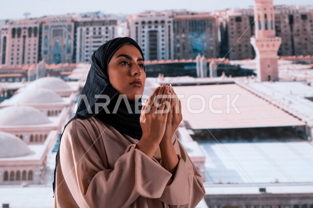 ثواب وفضل الدعاء في مسجد رسول الله, العمارة الإسلامية العريقة لقباب المساجد في المدينة المنورة, صورة مقربة لإمرأة عربية سعودية خليجية ترتدي عباءة ملونة تقف أمام المسجد النبوي الشريف وتدعو الله, خلفية القبب لمسجد النبي محمد عليه الصلاة والسلام