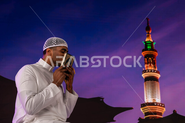 إيماءات تقبيل القرآن الكريم، فضل الصلاة و الدعاء في المسجد النبوي الشريف، قدوم المسلمين من شتى أنحاء العالم إلى الأماكن المقدسه في المدينة المنورة، رجل مسلم عربي سعودي يقوم بقراءة القرآن،  العبادة و التقرب إلى الله، خلفية المئذنة و المظلات الإلكترونيه