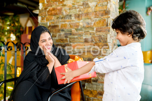 طفل عربي سعودي خليجي يحتفل بعيد الام و يقدم لوالدته هدية ، عيد أم سعيد ، عيد ميلاد ، قضاء الوقت و الاحتفال سويا بالمطعم بأجواء حماسية رائعة ، مطاعم وكافيهات السعودية