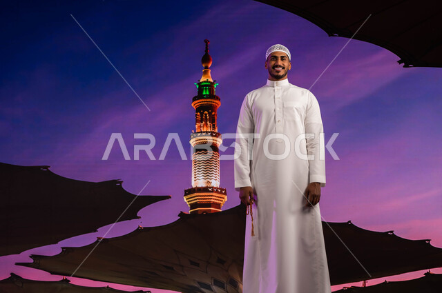 فضل الصلاة و الدعاء في مسجد رسول الله، قدوم المسلمين من شتى أنحاء العالم الى الأماكن المقدسه في المدينة المنورة، رجل مسلم مبتسم عربي سعودي خليجي يقف في ساحة المسجد النبوي، العبادة و التقرب إلى الله، خلفية المئذنة و المظلات الإلكترونيه