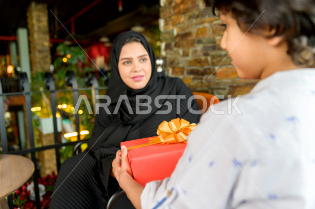 طفل عربي سعودي خليجي يحتفل بعيد الام و يقدم لوالدته هدية ، عيد أم سعيد ، عيد ميلاد ، قضاء الوقت و الاحتفال سويا بالمطعم بأجواء حماسية رائعة ، مطاعم وكافيهات السعودية