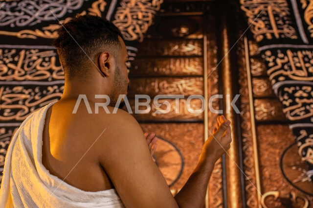 التذلل والطلب من الله تعالى, صورة من الخلف لحاج عربي سعودي خليجي يرتدي ثياب الإحرام يرفع يديه و يدعي بخشوع, فضل العمرة في شهر رمضان المبارك، أداء فريضة الحج و العمرة في شهر ذو الحجة, خلفية باب الكعبة الذهبي في الحرم المكي الشريف