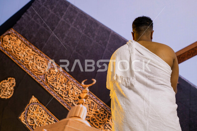 التضرع والخشوع إلى الله في المسجد الحرام, صورة من الخلف لرجل عربي سعودي خليجي يرتدي زي الإحرام يقف أمام الكعبة المشرفة في مكة المكرمة, صورة مقربة لميزاب الكعبة المشرفة, أداء فريضة الحج في ذو الحجة, فضل العمرة في شهر رمضان المبارك