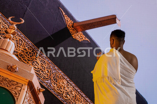 الدعاء والتوسل إلى الله في المسجد الحرام, صورة من الخلف لحاج عربي سعودي خليجي يرتدي زي الإحرام يقف أمام الكعبة المشرفة في مكة المكرمة, صورة مقربة لميزاب الكعبة المشرفة ومقام ابراهيم عليه السلام, أداء فريضة الحج في ذو الحجة, فضل العمرة في شهر رمضان المبارك