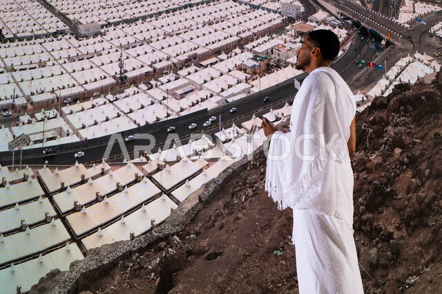 أماكن ومعالم اسلامية دينية مقدسة في مكة المكرمة, أداء الفرائض الدينية, صورة من الخلف لحاج من حجاج بيت الله الحرام يرتدي لباس الإحرام في مشعر منى، منظر علوي للخيام البيضاء في منى, اداء مناسك الحج والعمرة، العبادة والتقرب إلى الله , موسم الحج 2023