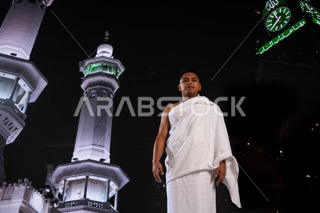 خلفية برج الساعة ومآذن الحرم المكي الشريف, الاجتهاد في الطاعات والتقرب الى الله تعالى  في الأشهر المباركة, فضل العمرة في شهر رمضان المبارك, شاب أندونيسي مسلم يرتدي لباس الإحرام، اداء مناسك الحج والعمرة, قدوم الحجاج من خارج السعودية