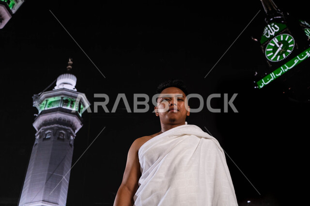 الاجتهاد في الطاعات والتقرب الى الله تعالى  في الأشهر المباركة, فضل العمرة في شهر رمضان المبارك, شاب أندونيسي مسلم يرتدي لباس الإحرام، اداء مناسك الحج والعمرة, قدوم الحجاج من خارج السعودية, خلفية برج الساعة ومآذن الحرم المكي الشريف
