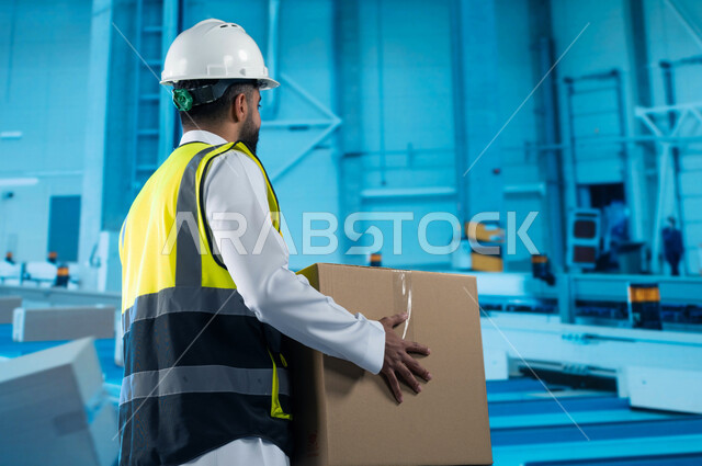 تسهيل عملية التعبئة والتغليف بامتلاك أحدث الأدوات والمعدات, تسريع عجلة الانتاج في مصانع التغليف باستخدام التكنولوجيا الحديثة, صورة من الخلف لمهندس عربي خليجي سعودي يحمل بيده صندوق كرتوني, انتشار الهندسة الصناعية في المملكة العربية السعودية.