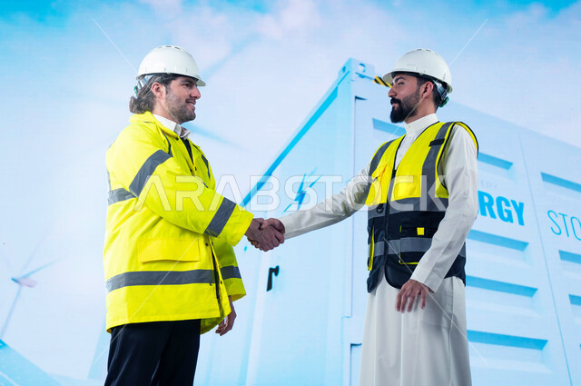 ايماءات المصافحة لنجاح عملية استخدام الطاقات البديلة, توفير وإنتاج الطاقه الكهربائية من الشمس والرياح, مهندسان عربيان سعوديان خليجيان مبتسمان, الإشراف والتدقيق على الألواح الشمسية و التوربينات الهوائية, خلفية مخزن الطاقة الكهربائية وتوربينات الرياح.