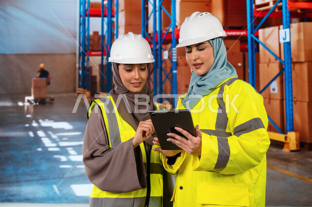 دمج التقنية و التكنولوجيا مع العمل, استخدم أجهزة التابلت للتأكد من وجود وتوفر البضاعة، عمليات ترتيب وتنظيم المستودعات المحلية، صورة مقربة لمسؤولات استلام عرب سعوديات خليجيات في قسم المخازن, خلفية صناديق وكراتين مغلفة.