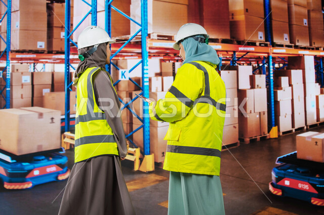 تحديد مستوى المخزون في المخازن، دمج التقنية و التكنولوجيا مع العمل, استخدم أجهزة التابلت للتأكد من وجود وتوفر البضاعة، صورة من الخلف لمسؤولات استلام عرب سعوديات خليجيات في قسم المخازن, خلفية صناديق وكراتين مغلفة.