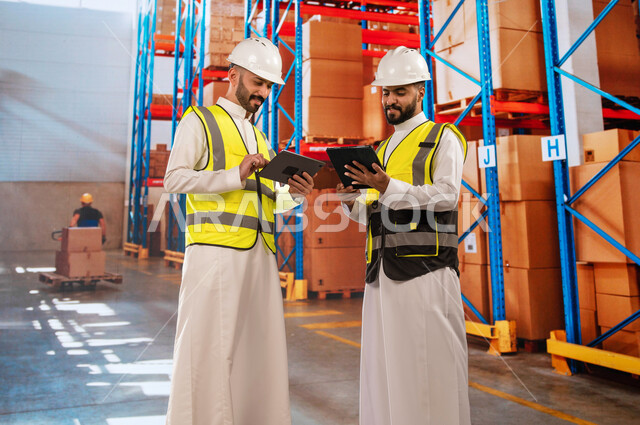 طلبيات و بضائع عربية سعودية خليجية، دمج التقنية و التكنولوجيا مع العمل, استخدم أجهزة التابلت للتأكد من وجود وتوفر البضاعة، عمال ترتيب وتنظيم المستودعات المحليه، مسؤولين استلام عرب سعودين خليجين في قسم المخازن, خلفية صناديق وكراتين مغلفة.