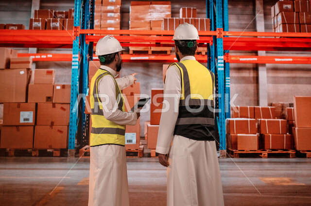 I use the tablet to ensure the presence and availability of the goods, workers arranging and organizing the local warehouses, Saudi Arabian Gulf goods and products, a back image of the officials receiving the Saudi Gulf Arabs in the warehouse department, 