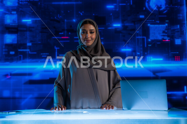 الاستثمار المالي والتجارة الالكترونية، تطوير الشركات والمشاريع الاقتصادية، سيدة أعمال عربية خليجية سعودية محجبة مبتسمة في مقر عملها بالشركة  تنظ إلى الكاميرا، خلفية شاشات هولوجرامية ثلاثية الأبعاد.