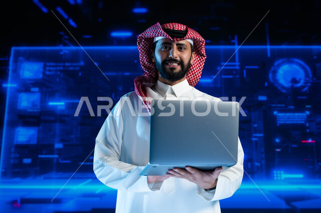 الاستثمار المالي والتجارة الالكترونية، تطوير الشركات والمشاريع الاقتصادية، سيد أعمال عربي خليجي سعودي مبتسم يرتدي الثوب السعودي التقليدي في مقر عمله بالشركة يحمل جهاز الحاسوب  ينظر إلى الكاميرا، خلفية شاشات هولوجرامية ثلاثية الأبعاد.