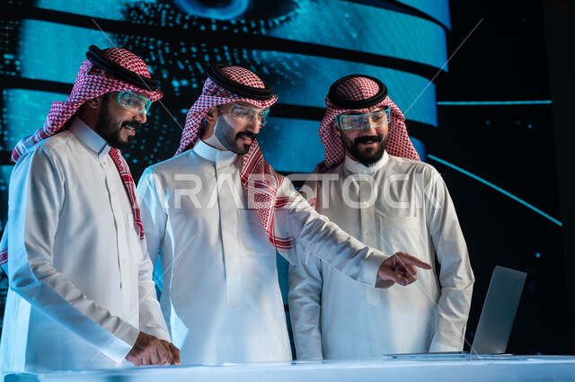 إجراء صفقات عمل في شركات التقنية والتكنولوجيا المستقبلية الحديثة, مجموعة من رجال أعمال عرب سعوديين خليجيين يرتدون الزي السعودي التقليدي ونظارات الواقع الافتراضي, خلفية شاشات هولوجرامية ثلاثية الأبعاد للذكاء الاصطناعي، رؤية مستقبيلة ٢٠٣٠.